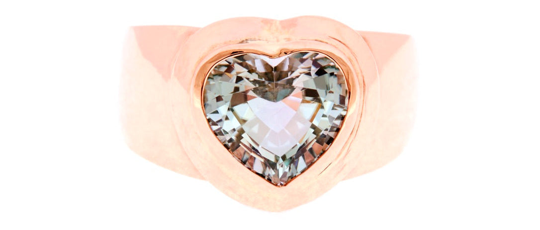 A rose gold ring featuring a large, heart-shaped clear gemstone in a prong setting, shown against a solid white background.
